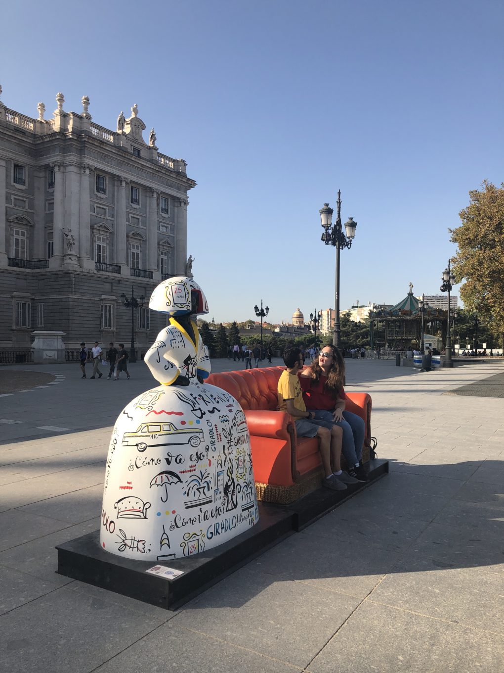 Personas sentadas en sofa al lado de figura de menina en Plaza de Oriente