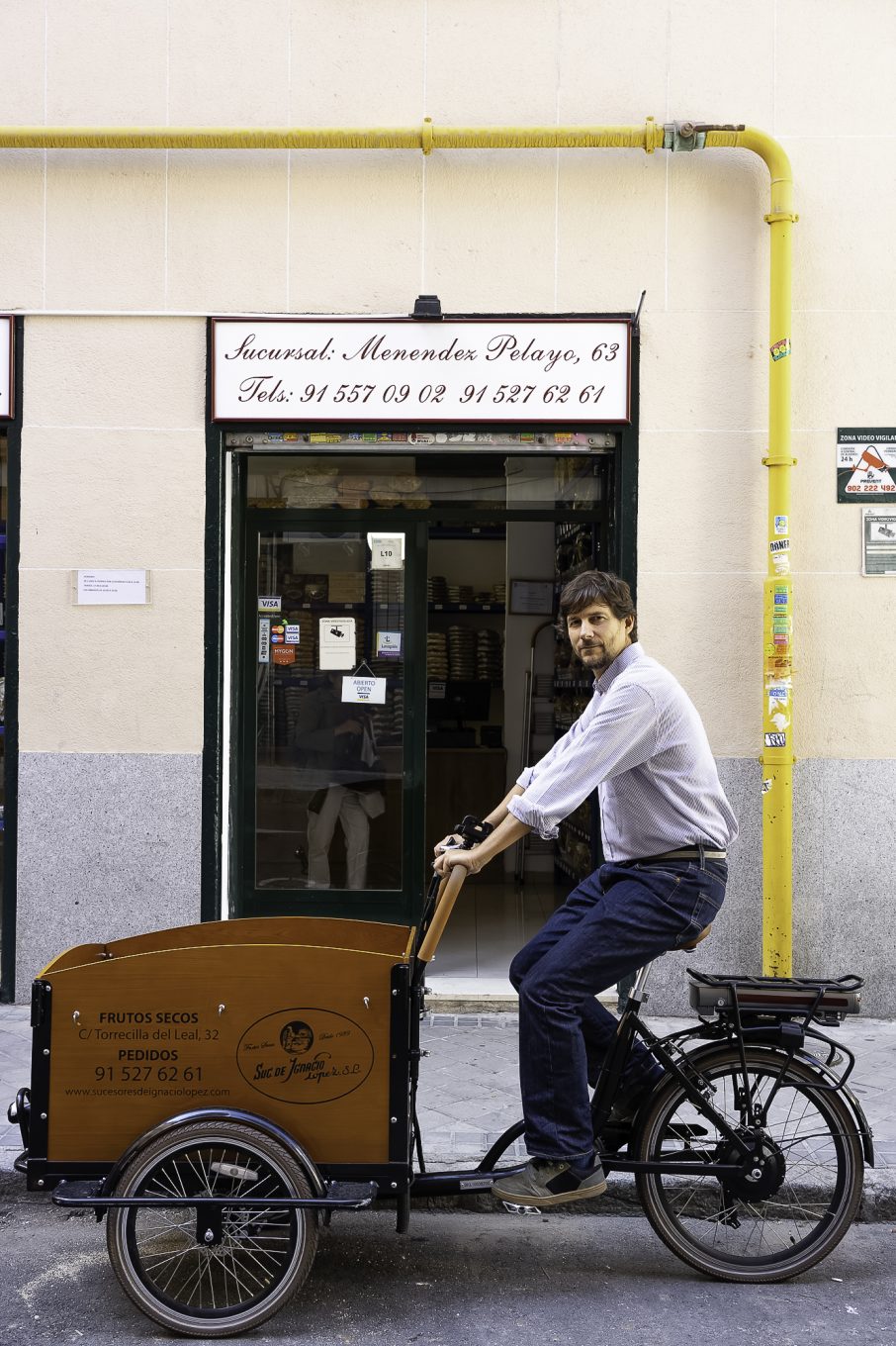 Hombre montado en triciclo de reparto delante de tienda