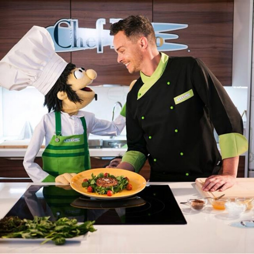 Cocinero con títere de gomaespuma en cocina presentando un plato