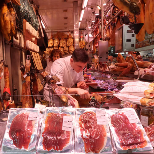 Hombre cortando jamón en puesto de charcutería