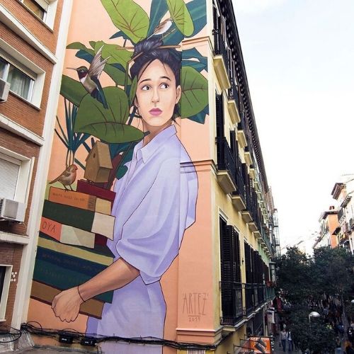 Mural de mujer acarreando libros y planta en fachada de edificio