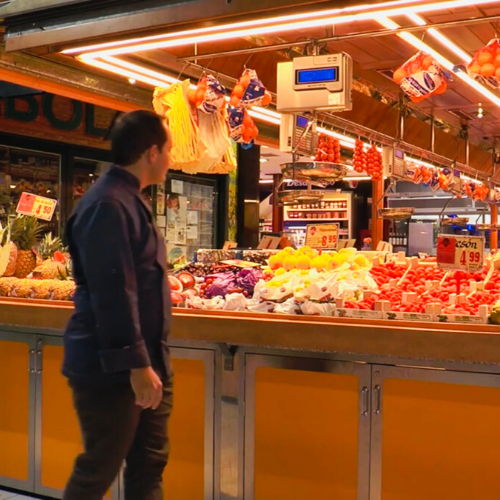 Hombre pasando por delante de puesto de frutería en mercado