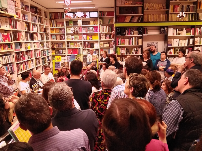 Gente de pie escuchando a escritor sentado en interior de librería